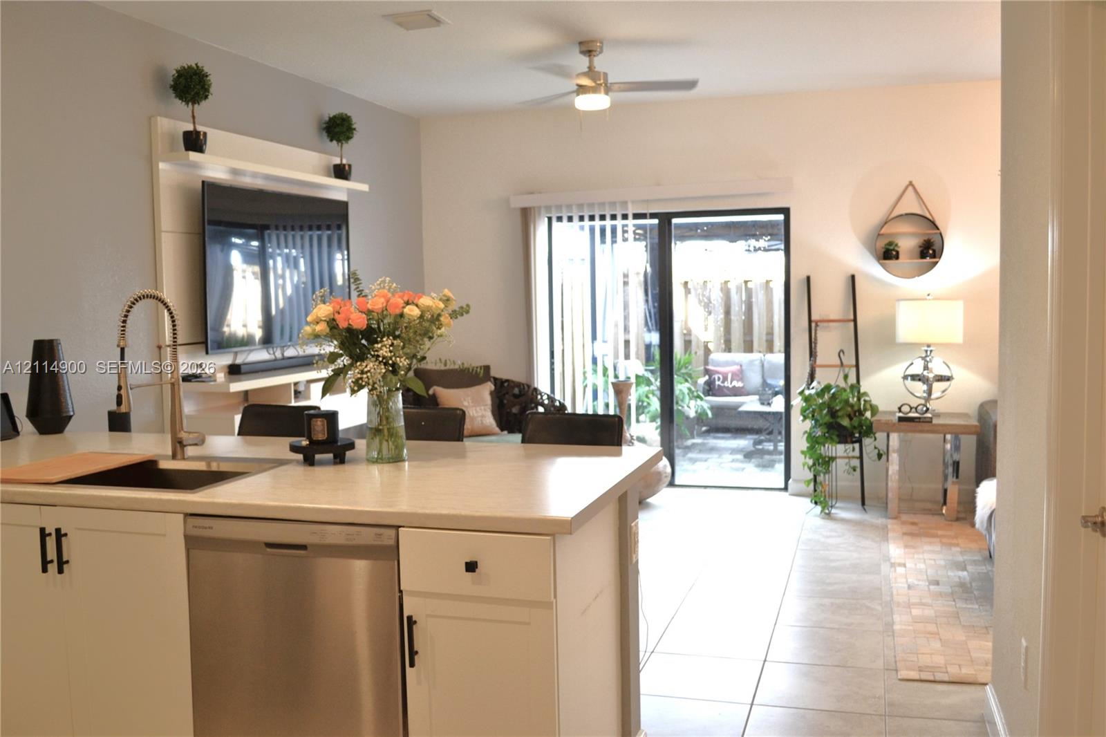 Kitchen island featuring a stainless steel dishwasher, undermount sink, and high-arc faucet, accompanied by a built-in entertainment center with integrated shelving, tile flooring, and sliding glass patio doors