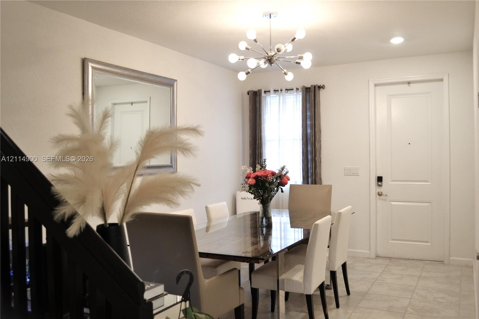 Open-concept interior featuring light-toned tile flooring, a multi-arm metallic sputnik-style chandelier, and a panelled entry door