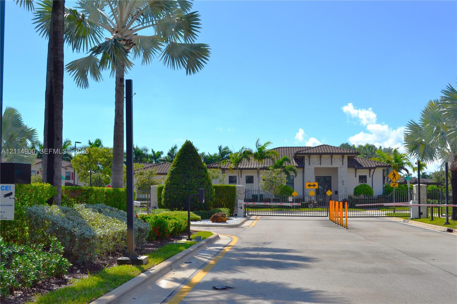 Gated community entrance featuring stone-accented architecture, tile roof, and professional landscaping with palm trees