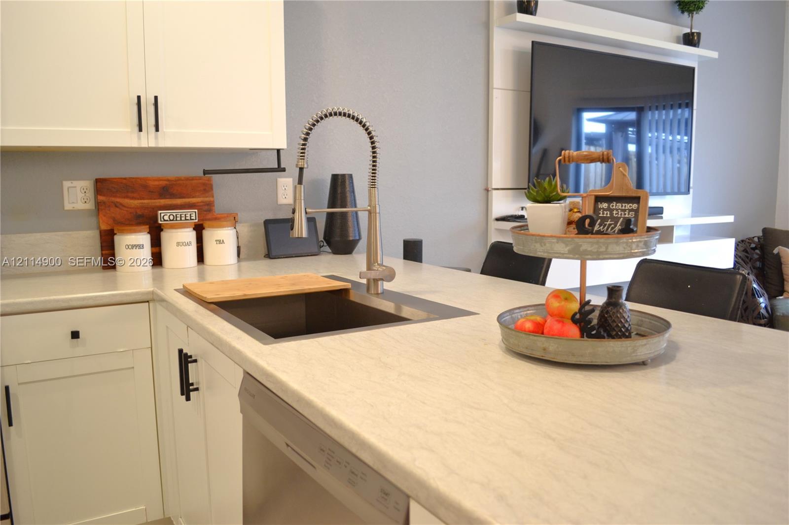Kitchen featuring white shaker-style cabinetry, a stone-finish countertop, an undermount sink with a gooseneck industrial faucet, a built-in dishwasher, and a wall-mounted display shelf