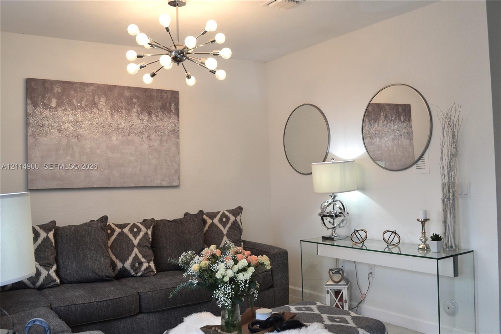 Sputnik-style multi-bulb chandelier with a polished chrome finish, two circular wall-mounted mirrors with metallic frames, and neutral interior wall paint