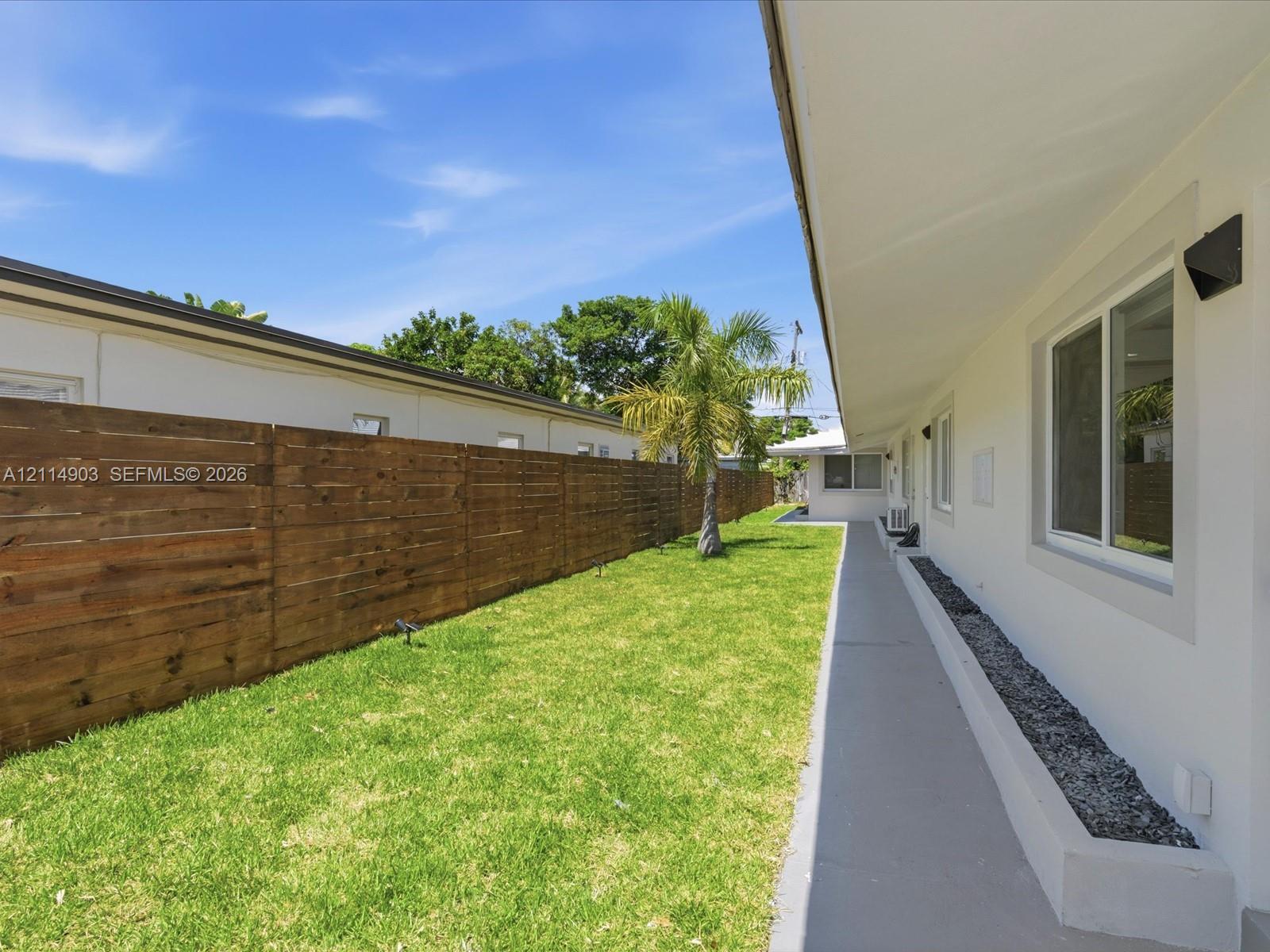 Exterior side yard featuring a concrete walkway, horizontal wood fencing, and a stone-filled planting border