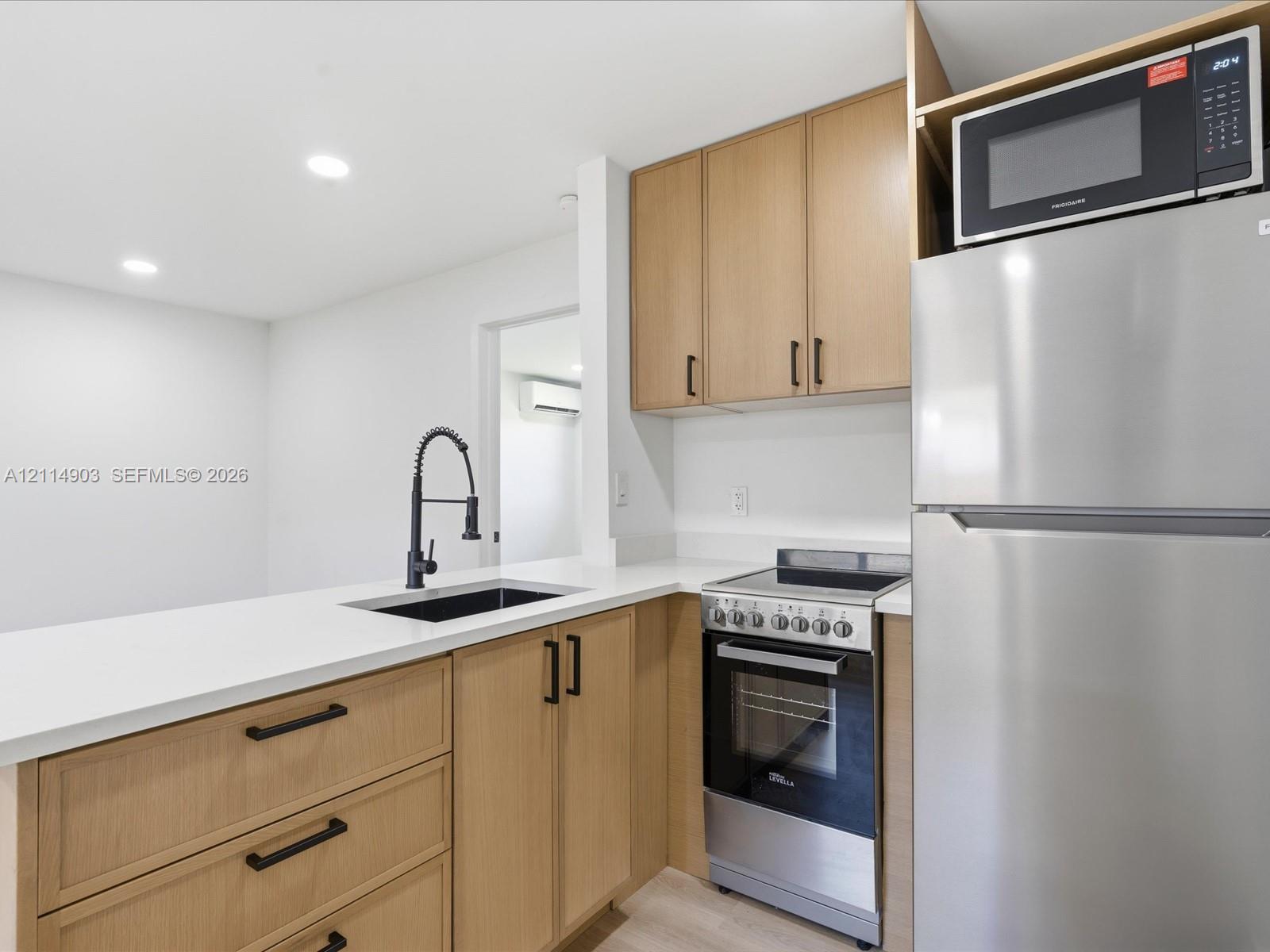 Kitchen featuring light wood-finish cabinetry, white countertops, a stainless steel refrigerator, a built-in microwave, and a matte black pulldown faucet