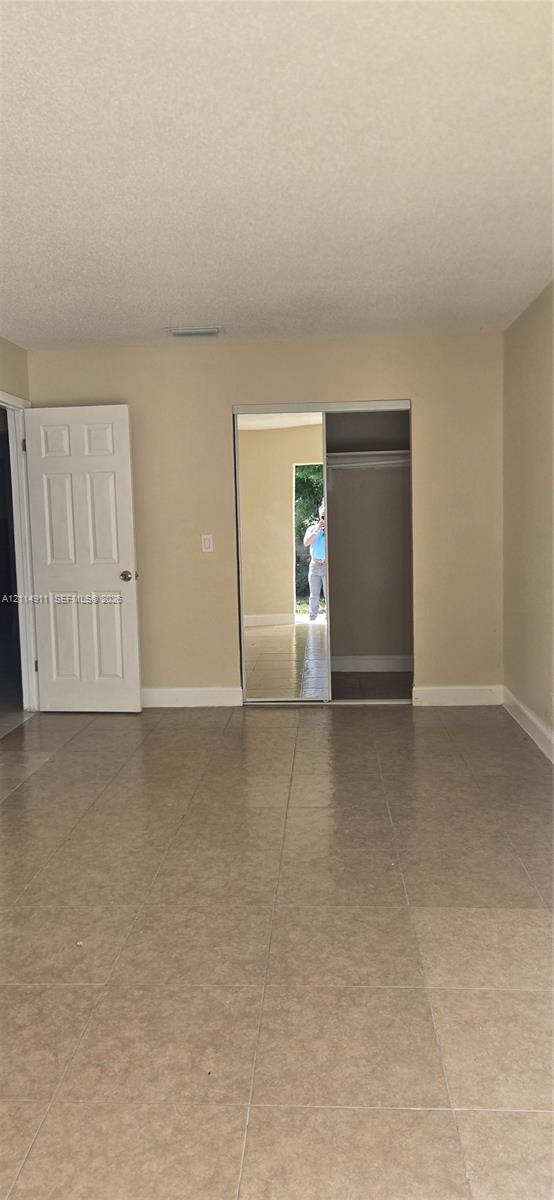 Room featuring neutral-toned tile flooring, a six-panel door, and a reach-in closet with sliding mirrored doors