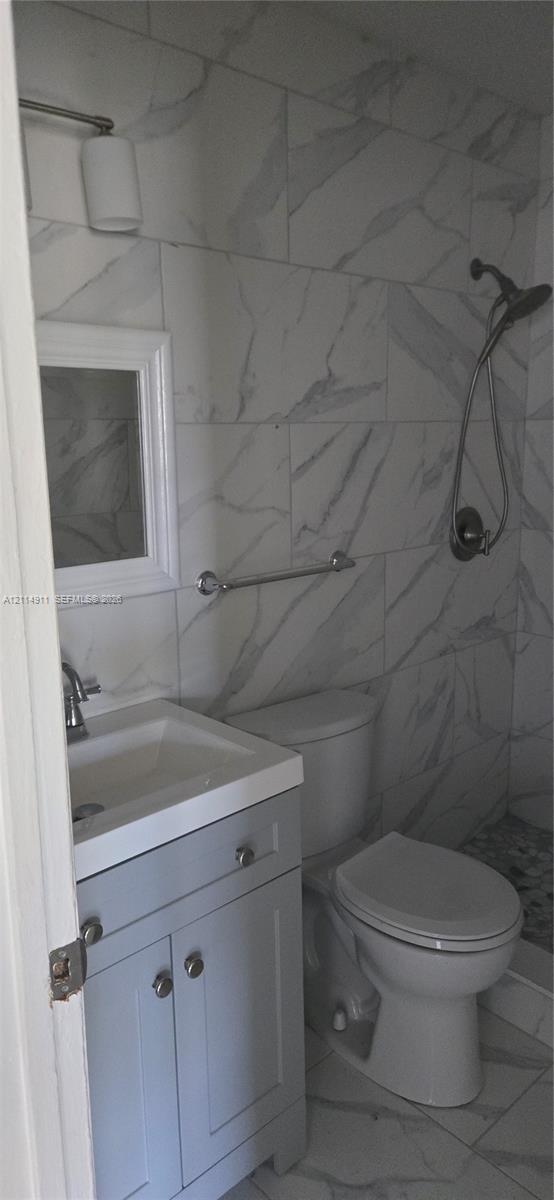Full-height stone-patterned wall tile, gray shaker-style vanity with white porcelain sink, chrome handheld shower fixture, and polished chrome hardware