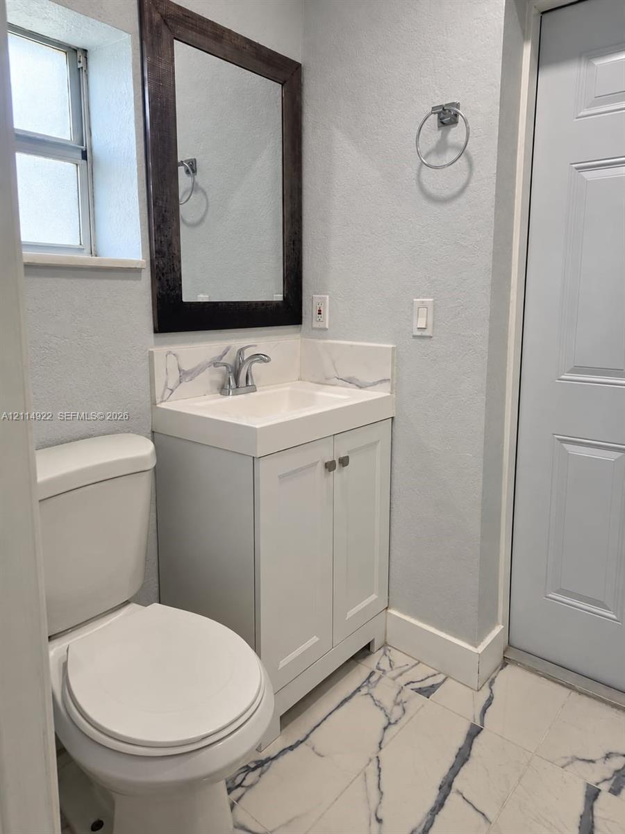 White vanity featuring a solid surface countertop with integrated sink and backsplash, dark-framed wall mirror, and patterned tile flooring