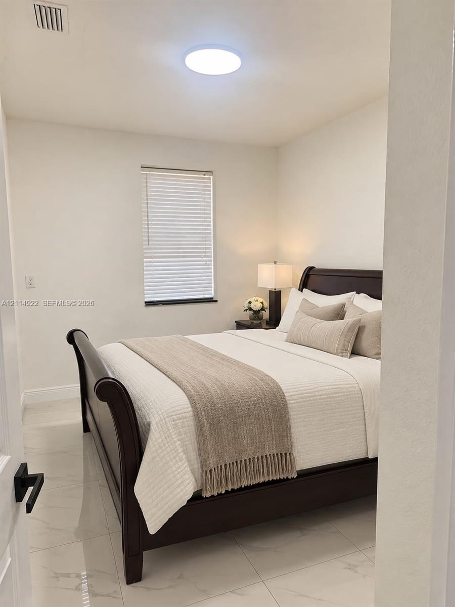 Interior room featuring polished tile flooring, neutral wall tones, a single window with horizontal blinds, and a circular flush-mount ceiling light fixture