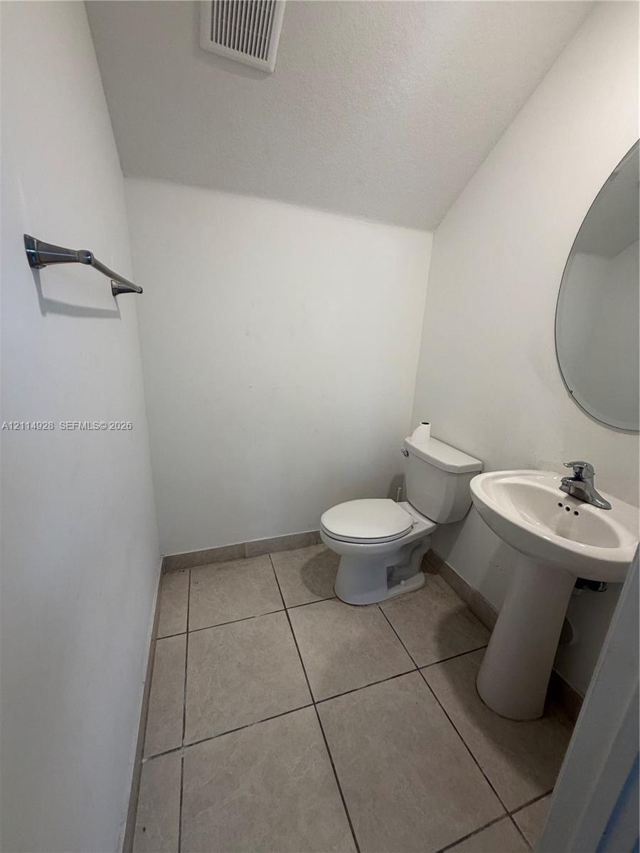 Powder room featuring tile flooring, a pedestal sink with a chrome single-handle faucet, an oval wall-mounted mirror, and a chrome towel bar
