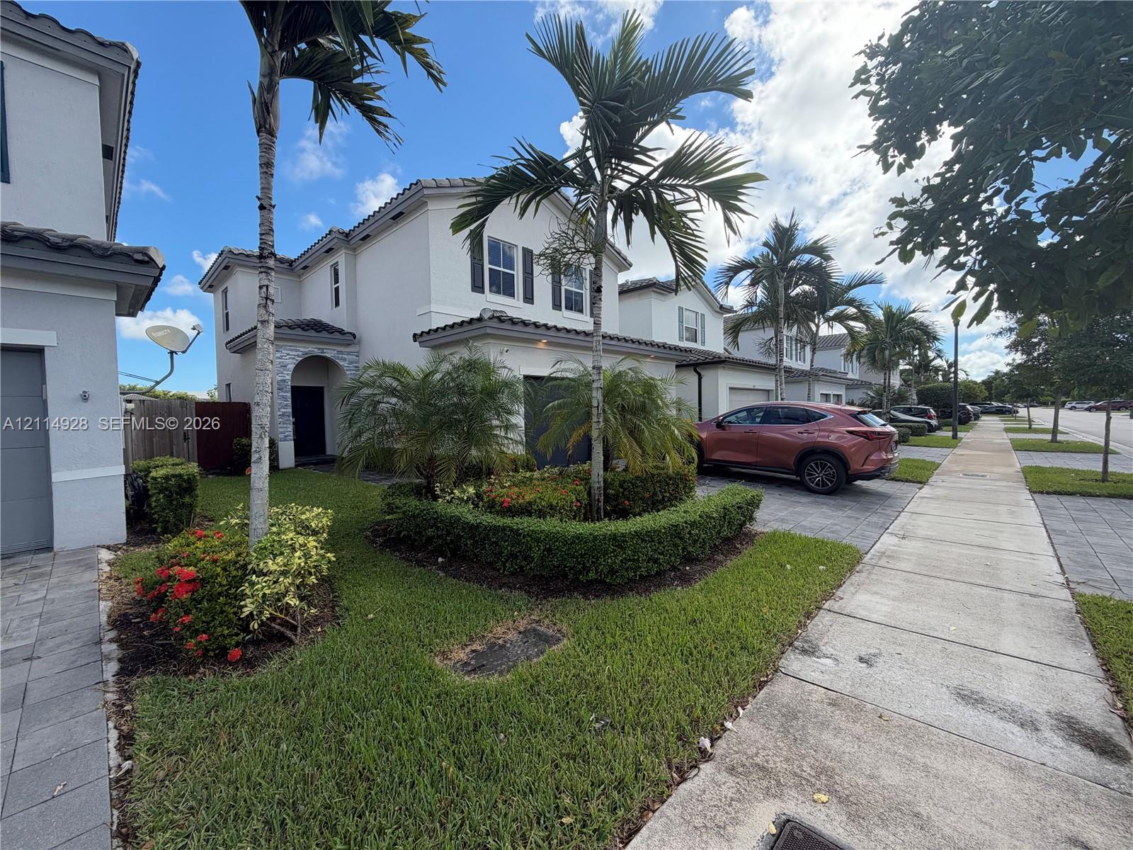 Two-story exterior featuring a light-colored stucco facade, decorative stone detailing at the entryway, shutter-framed windows, and professional landscaping with palm trees