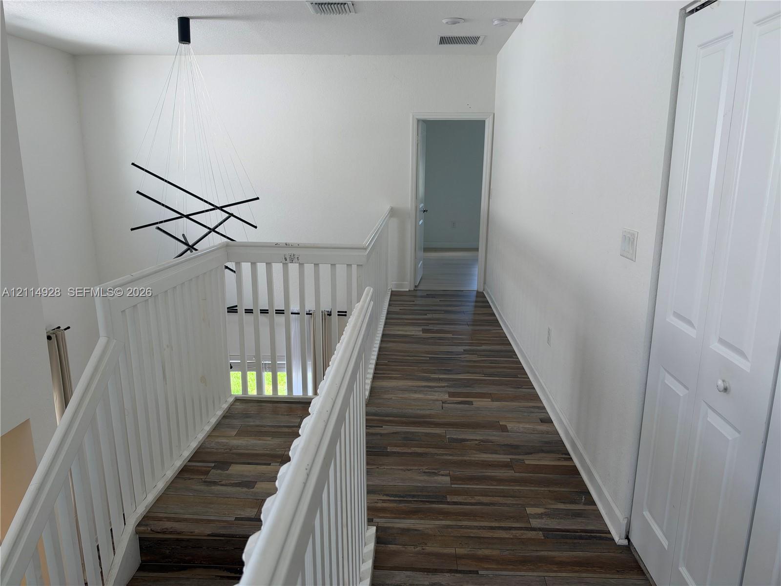 Hallway featuring wood-finish flooring, white railing, modern multi-rod pendant lighting, and a bifold closet