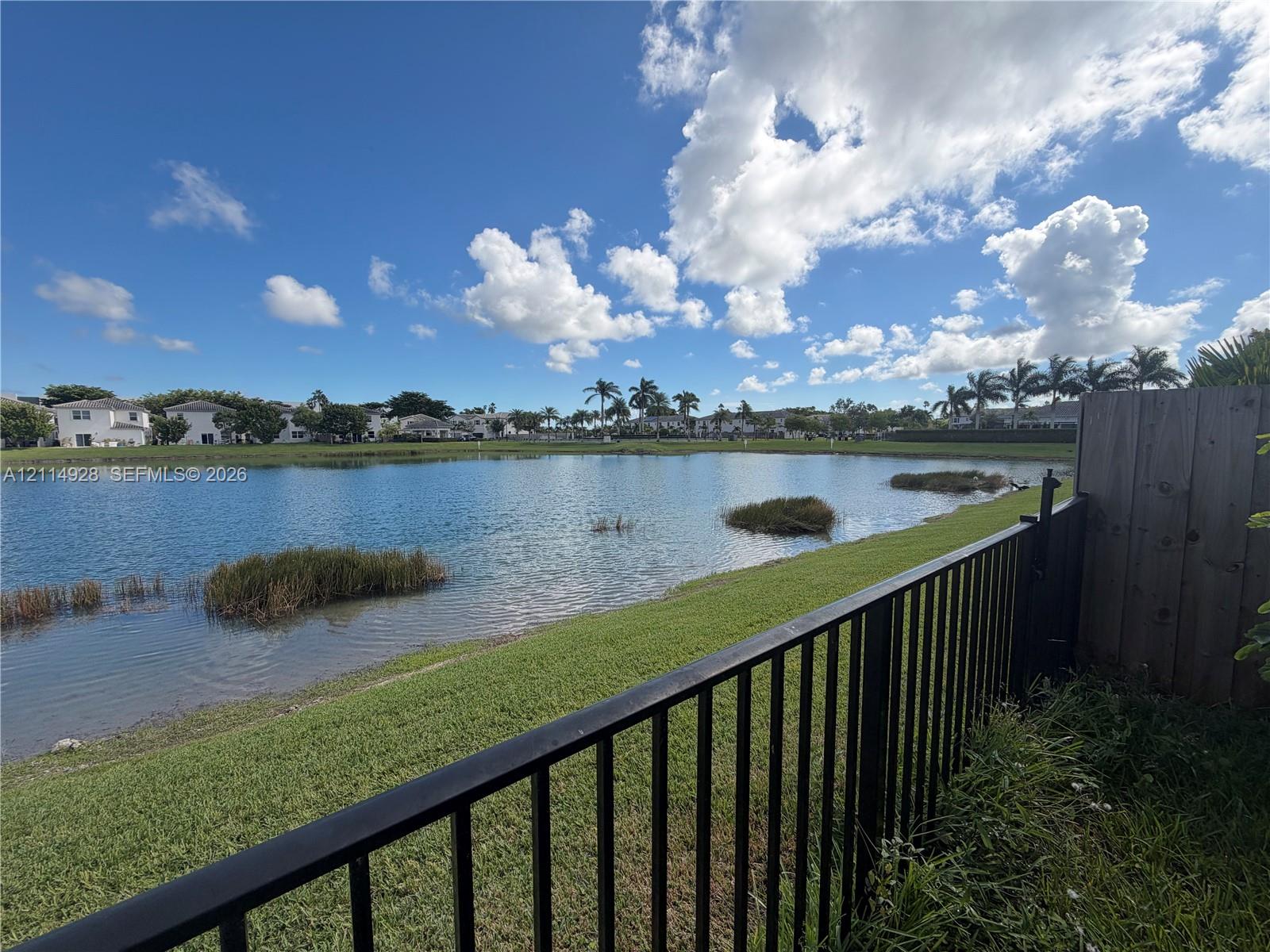 Waterfront lot featuring a manicured lawn, perimeter metal fencing, and wood-paneled privacy screening