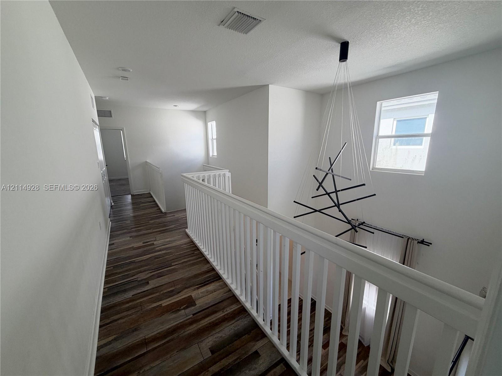 Wood-finish flooring, white spindle railing, and modern multi-arm chandelier