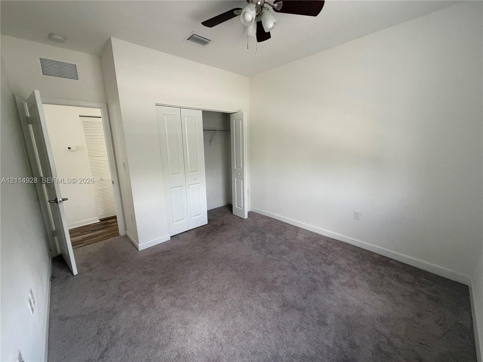 Neutral carpeted flooring, closet with bi-fold doors, and a ceiling-mounted light fixture with a fan