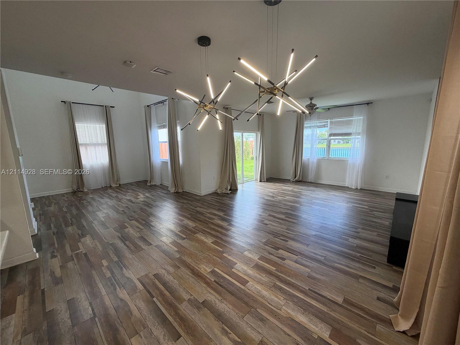 Open-concept interior featuring wood-finish flooring, high ceilings, dual geometric multi-arm pendant light fixtures, and large sliding glass doors providing access to the outdoors