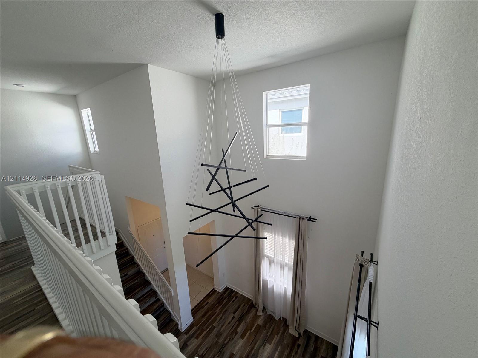 Two-story foyer featuring high ceilings, wood-finish flooring, a contemporary geometric multi-light chandelier, and white wooden balustrades