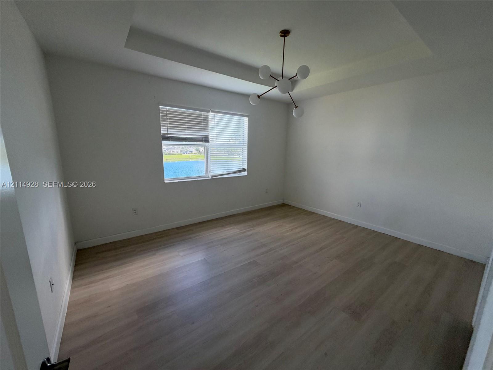 Tray ceiling, modern multi-arm chandelier, wood-finish flooring, and horizontal window blinds