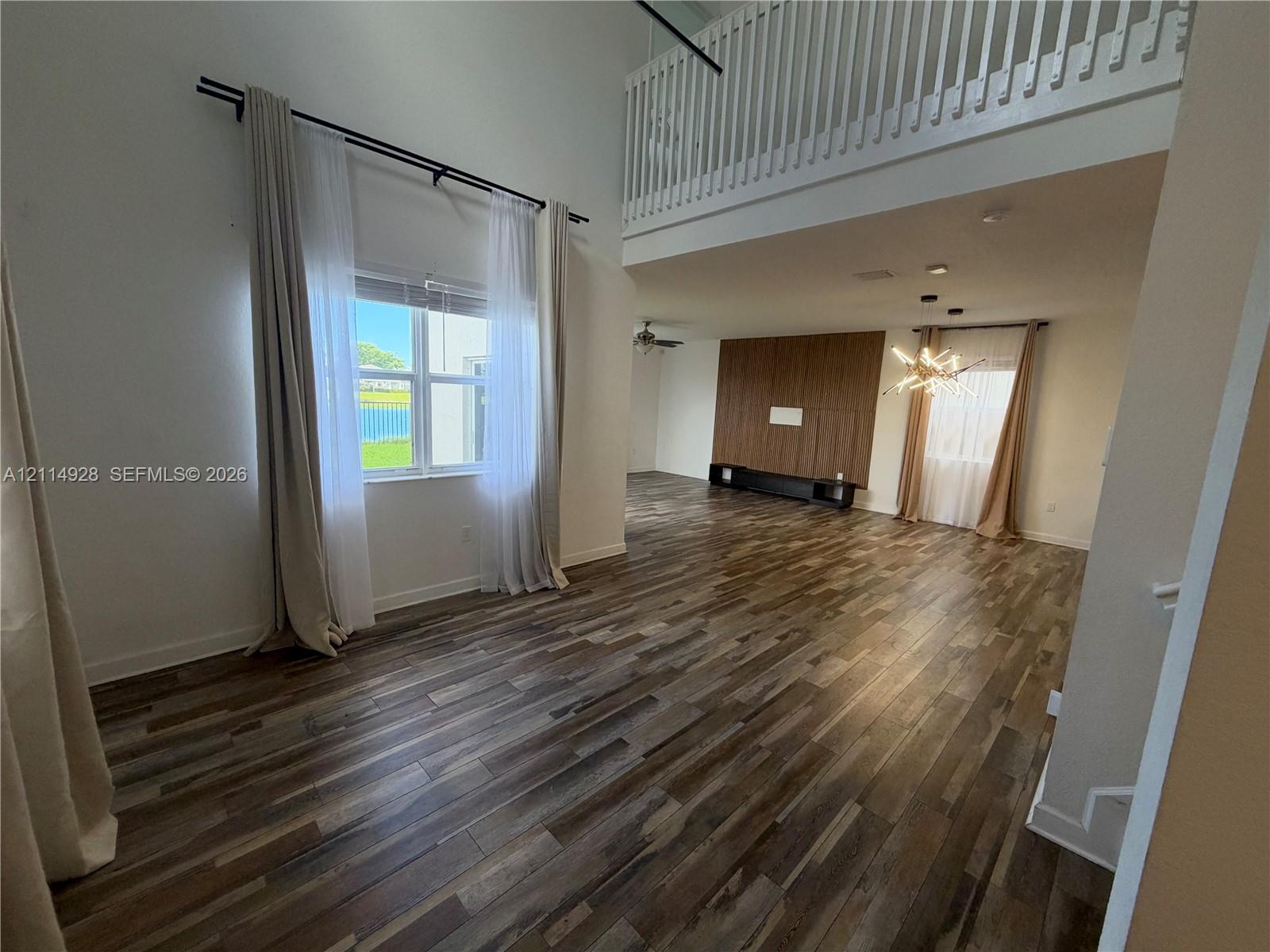 Interior featuring double-height ceilings, wood-finish flooring, a wood-panel accent wall, and a slatted staircase railing