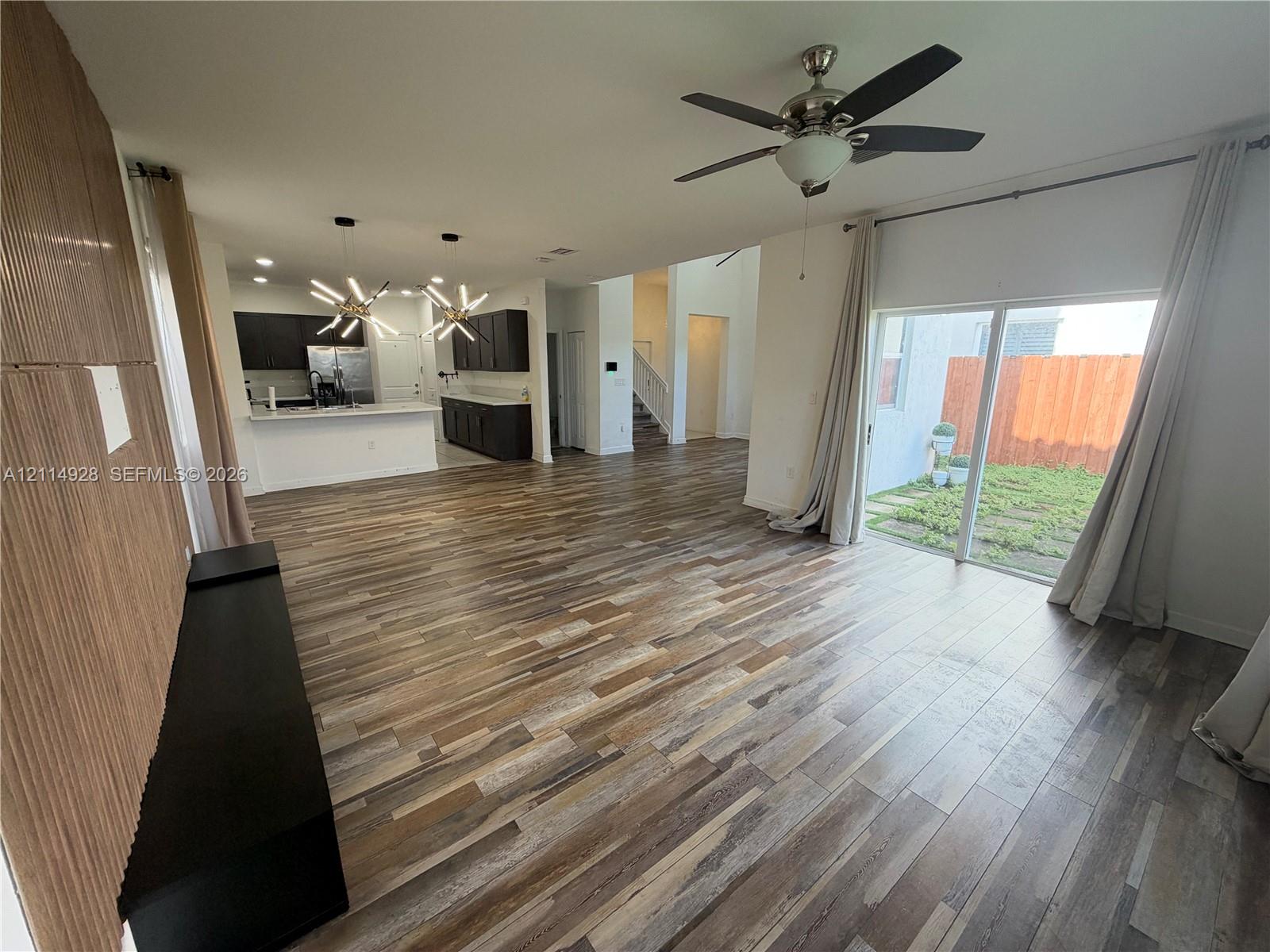 Wood-finish flooring throughout, kitchen featuring dark cabinetry and a peninsula, modern geometric pendant lighting, ceiling fan, and sliding glass doors