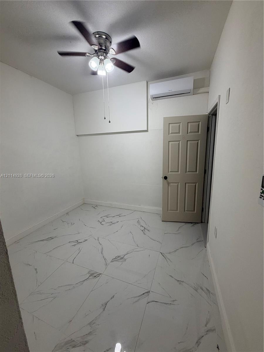 Large-format tile flooring featuring a marble-style pattern, ceiling fan with integrated lighting, and wall-mounted ductless climate control unit