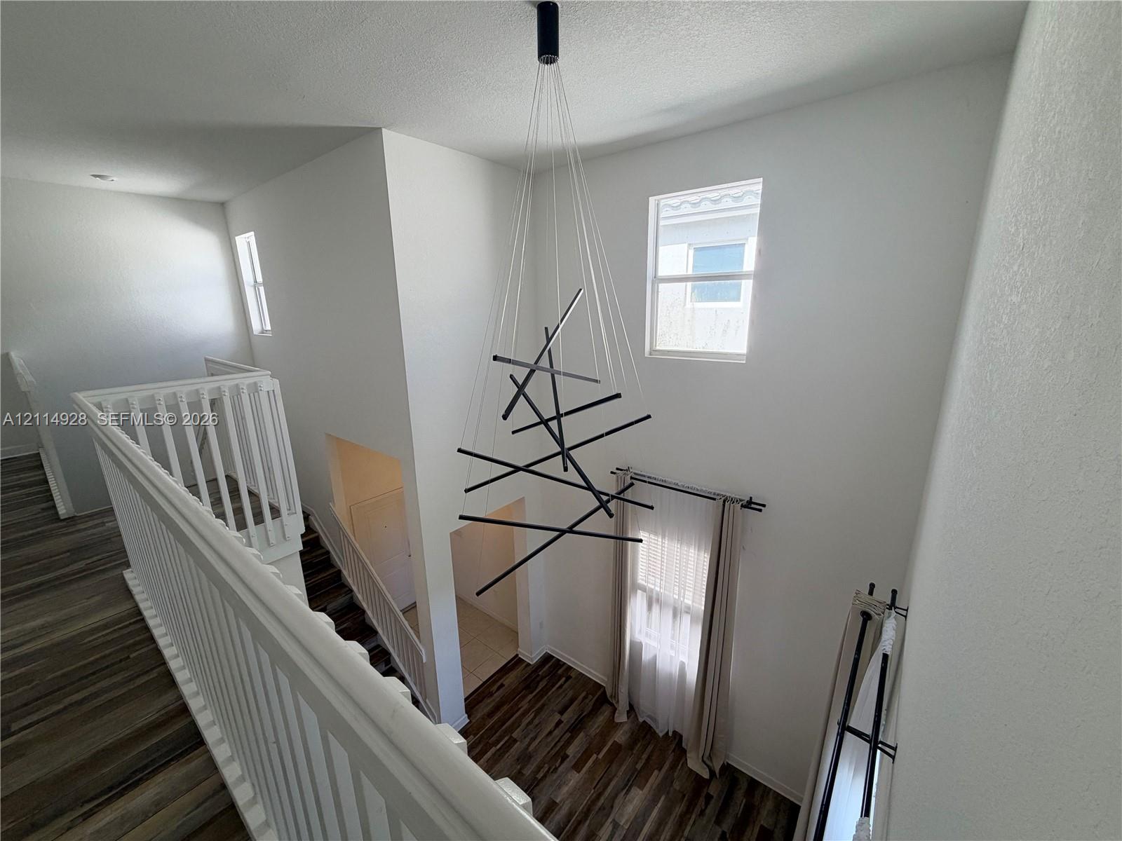 High-ceilinged entry featuring wood-finish flooring, a contemporary geometric chandelier, and white railings