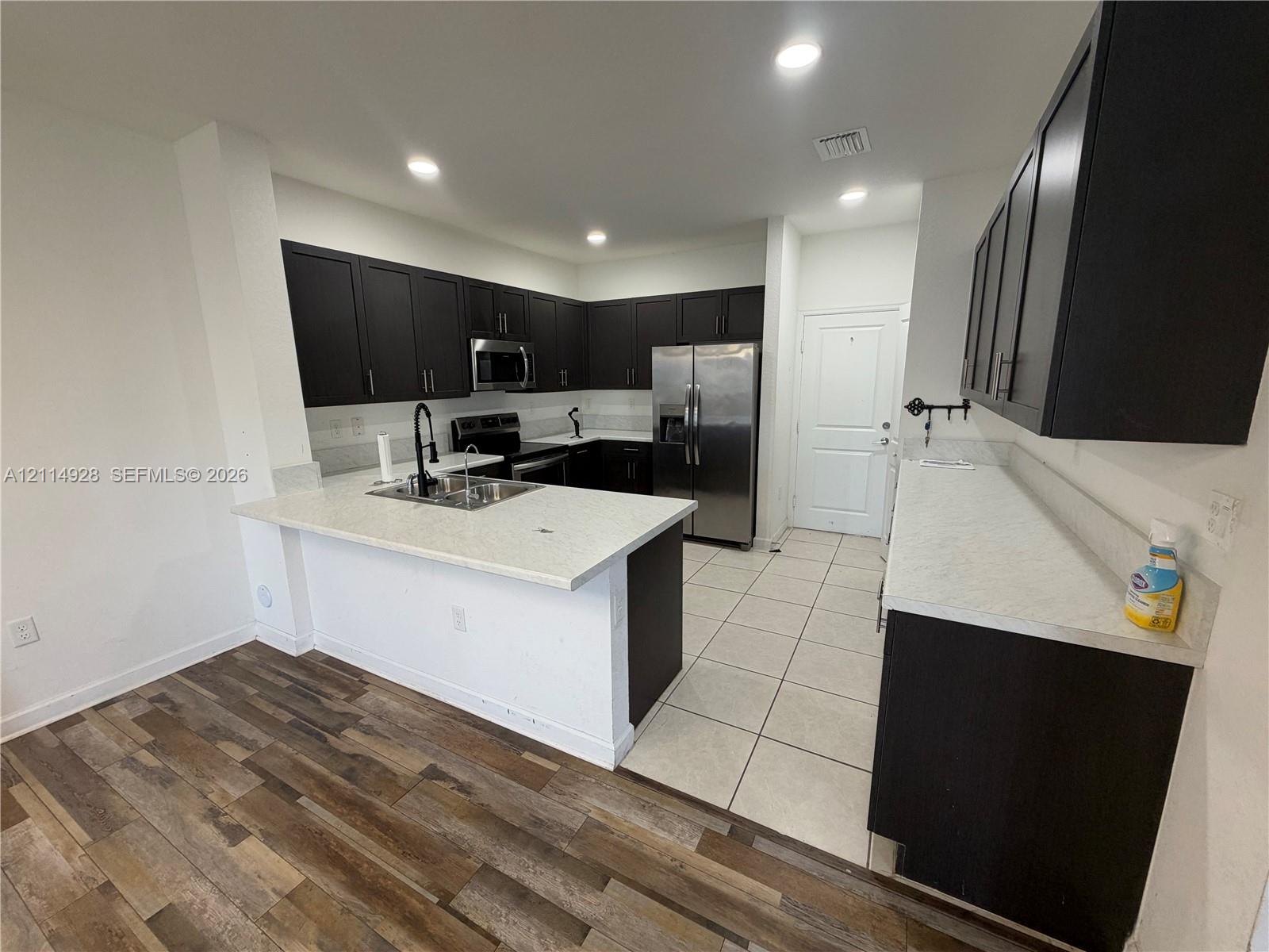 Kitchen featuring dark cabinetry, stone-finish countertops, stainless steel appliances, recessed lighting, and a combination of wood-finish and tile flooring