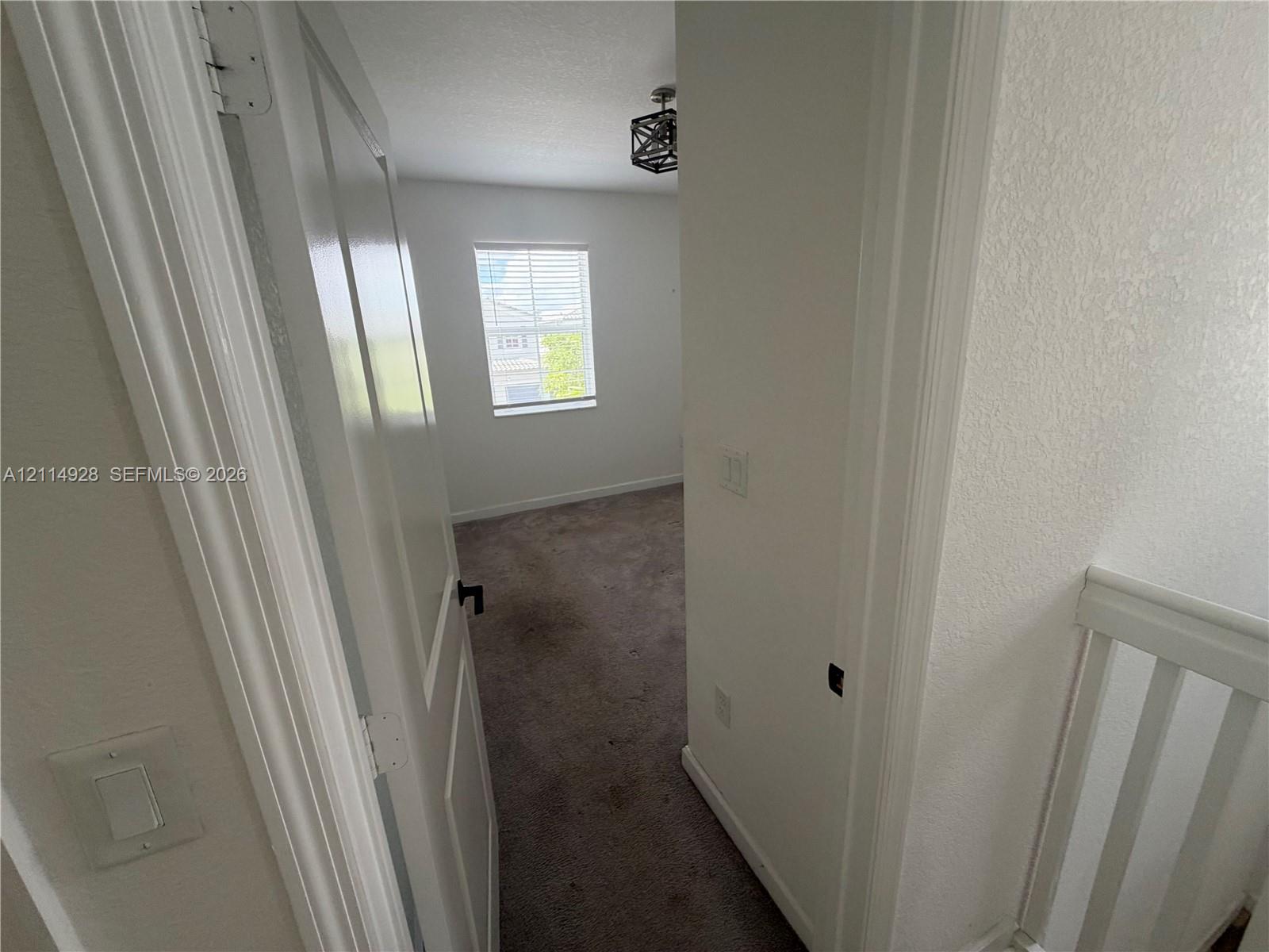Interior space featuring neutral-toned carpeting, a geometric metal chandelier, a singular window with horizontal blinds, and a solid-panel door