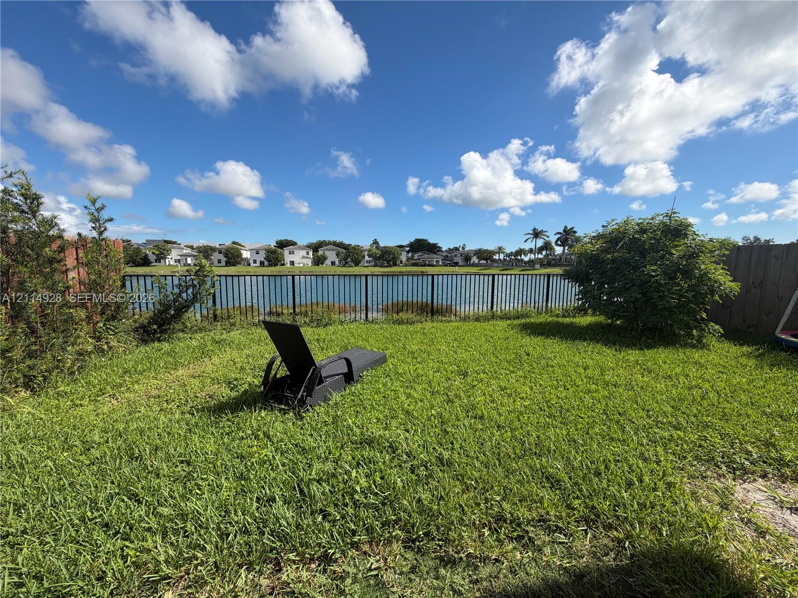 Backyard featuring a grass lawn, metal perimeter fencing, and water frontage