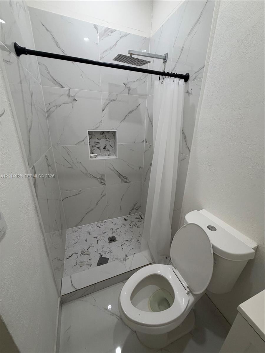 Shower featuring large-format veined tile surround, recessed wall niche, rain-style shower head, and matte black hardware
