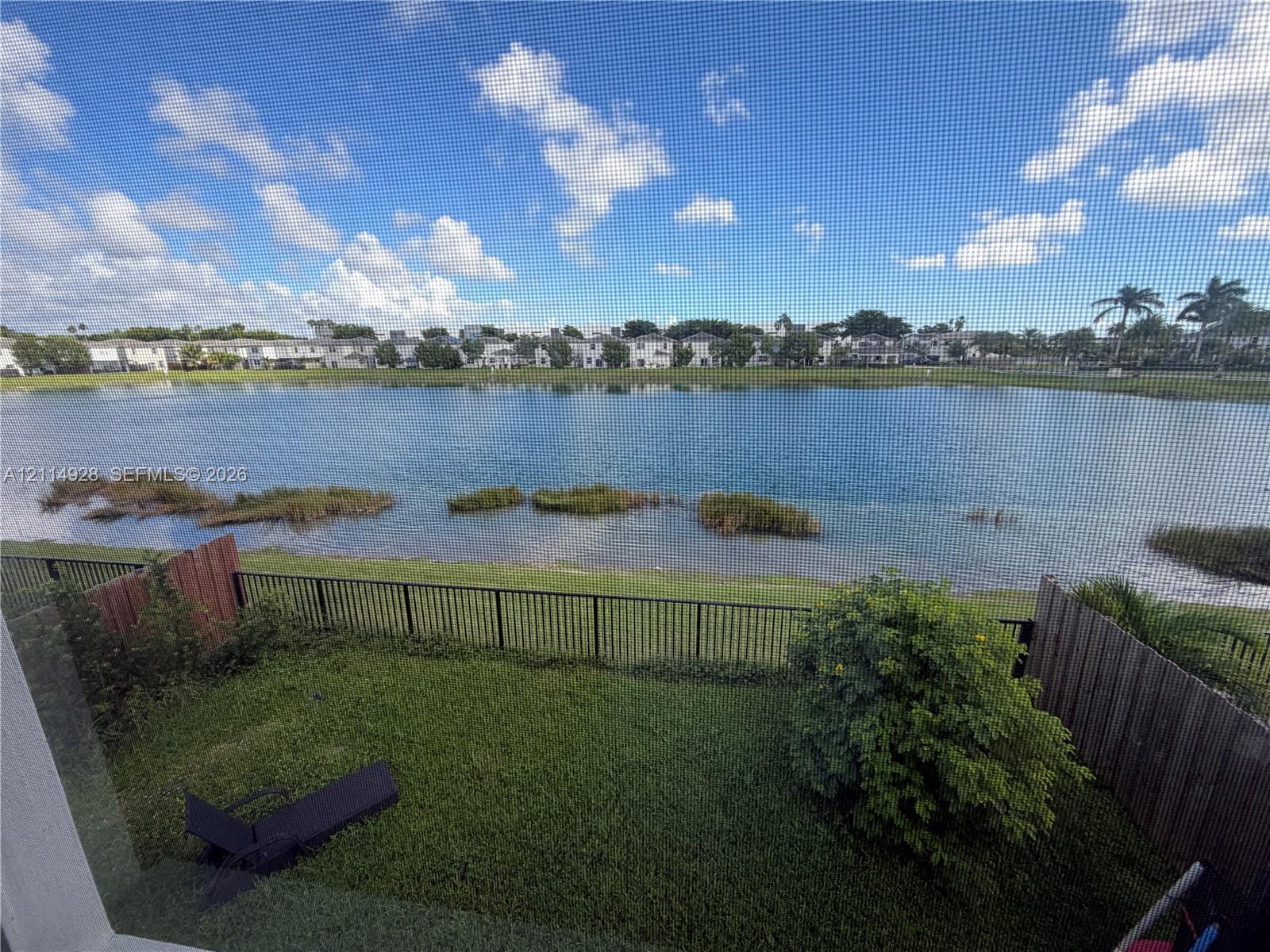 Waterfront property featuring a grass lawn, perimeter metal fencing, and wood-paneled privacy partitions