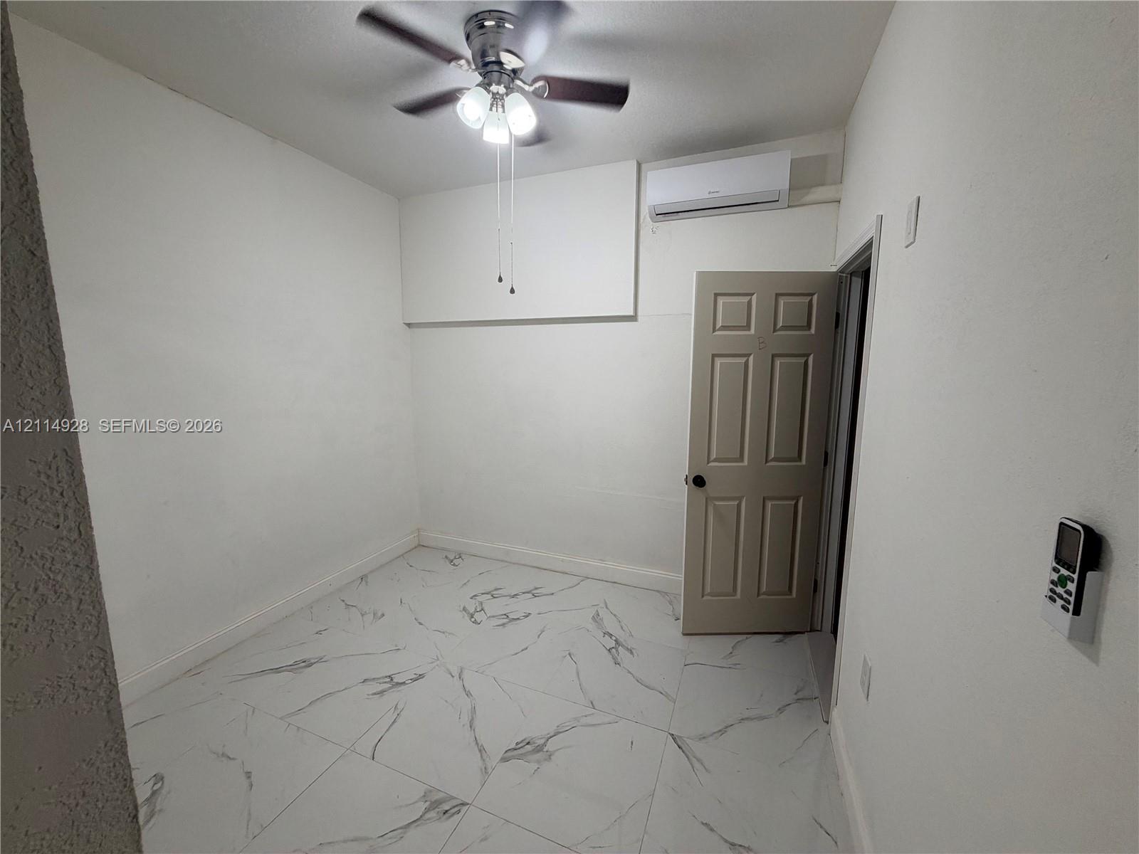 Large-format stone-style tile flooring, ceiling fan with integrated lighting, and wall-mounted ductless climate control system