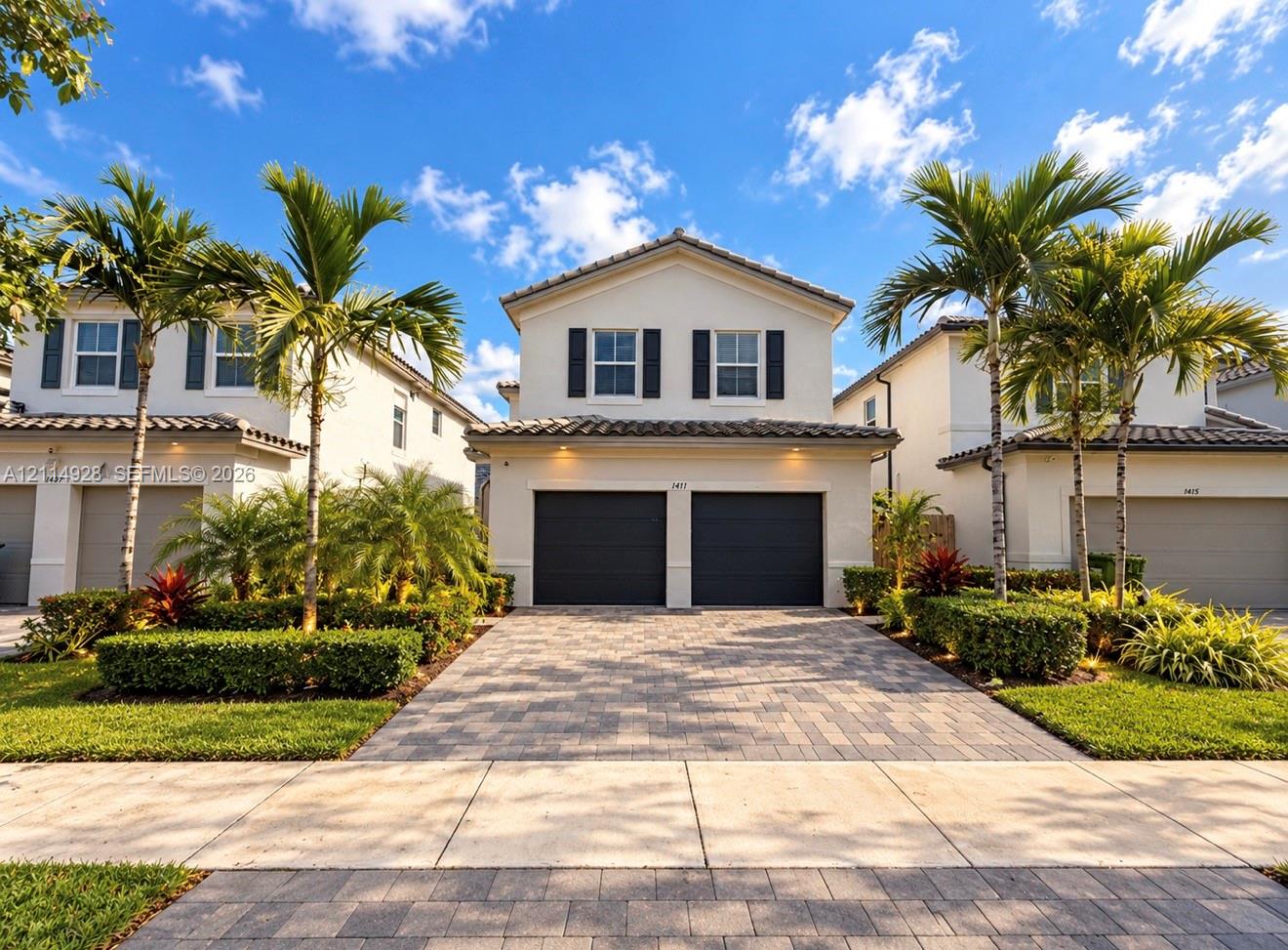 Two-story exterior featuring a stucco facade, concrete tile roof, paver driveway, two-car garage, and shuttered windows