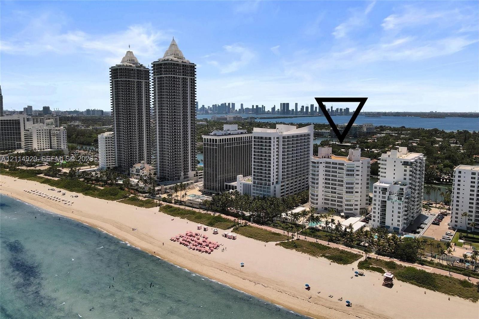 High-rise building featuring a white facade, direct beach frontage, and a pool area with mature palm trees