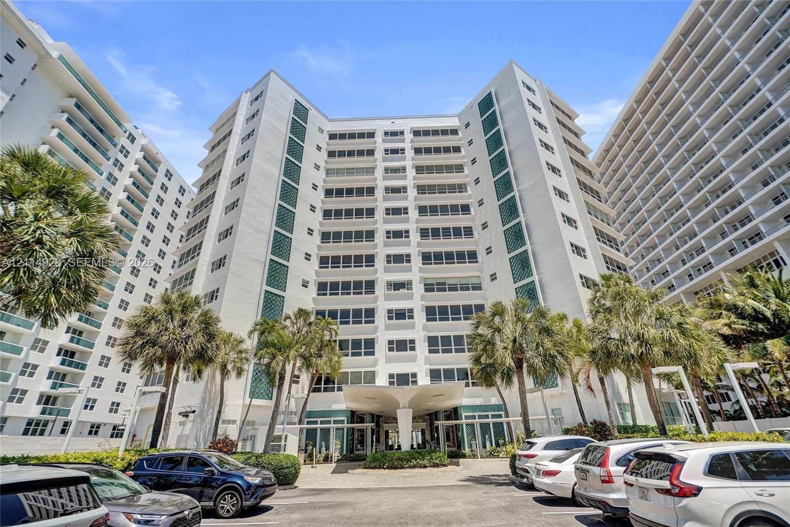 High-rise residential exterior featuring a white concrete facade, multi-story glass-enclosed balconies, and a distinctive structural porte-cochre entry