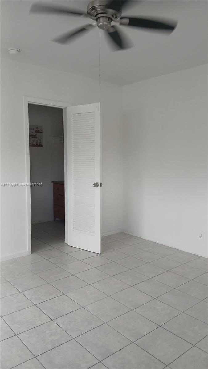 Neutral-toned tile flooring, ceiling fan with multi-blade design, and interior louvered door