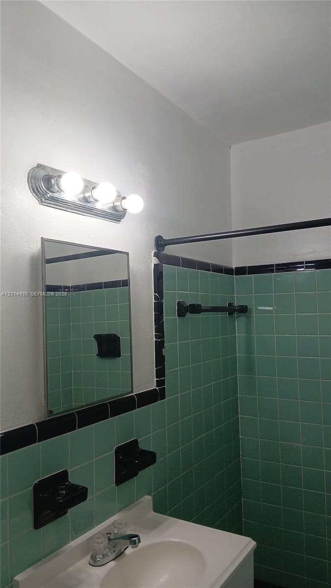 Wall-mounted three-bulb chrome light fixture, rectangular medicine cabinet, integrated sink vanity, and custom green wall tile with black trim accents
