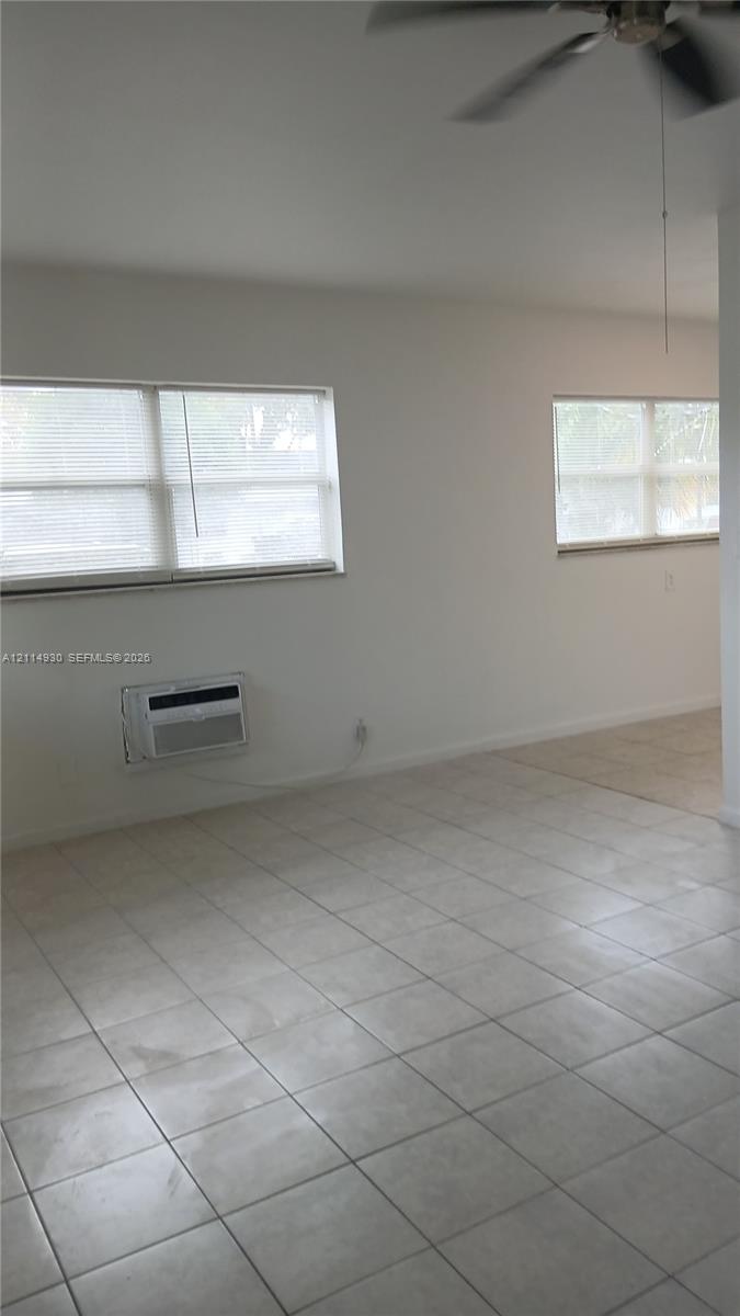 Ceramic tile flooring, dual windows with blinds, ceiling fan, and wall-mounted cooling unit