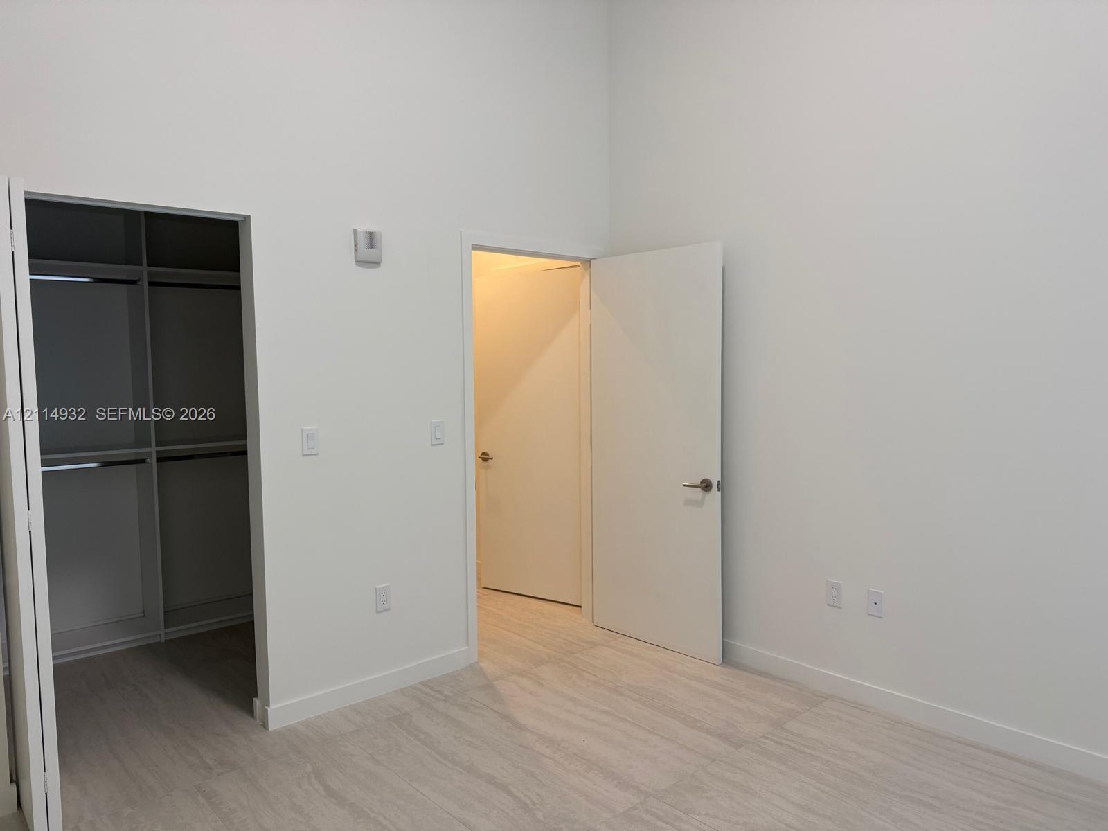 High-ceilinged room featuring light-toned wood-finish flooring, white walls, built-in closet shelving, and solid-core doors with brushed-metal hardware