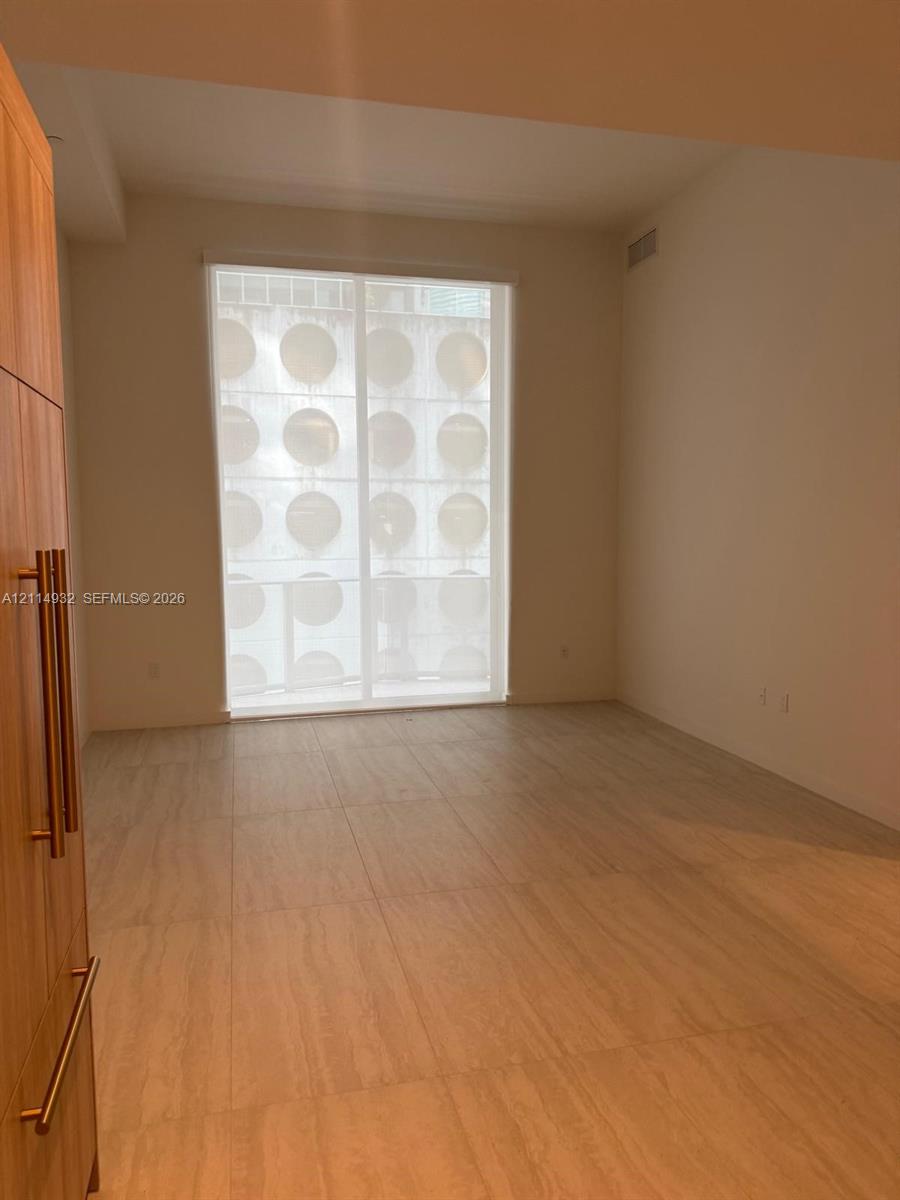 Large-format tile flooring, floor-to-ceiling window with privacy screen, and built-in wood-finish cabinetry featuring vertical bar pulls