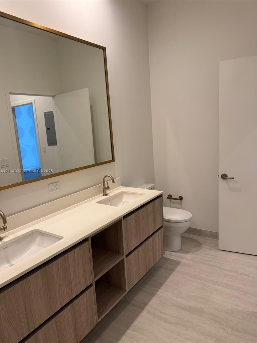 Floating wood-finish vanity with a double-basin countertop, undermount sinks, brass-toned fixtures, and a large rectangular mirror with a matching frame