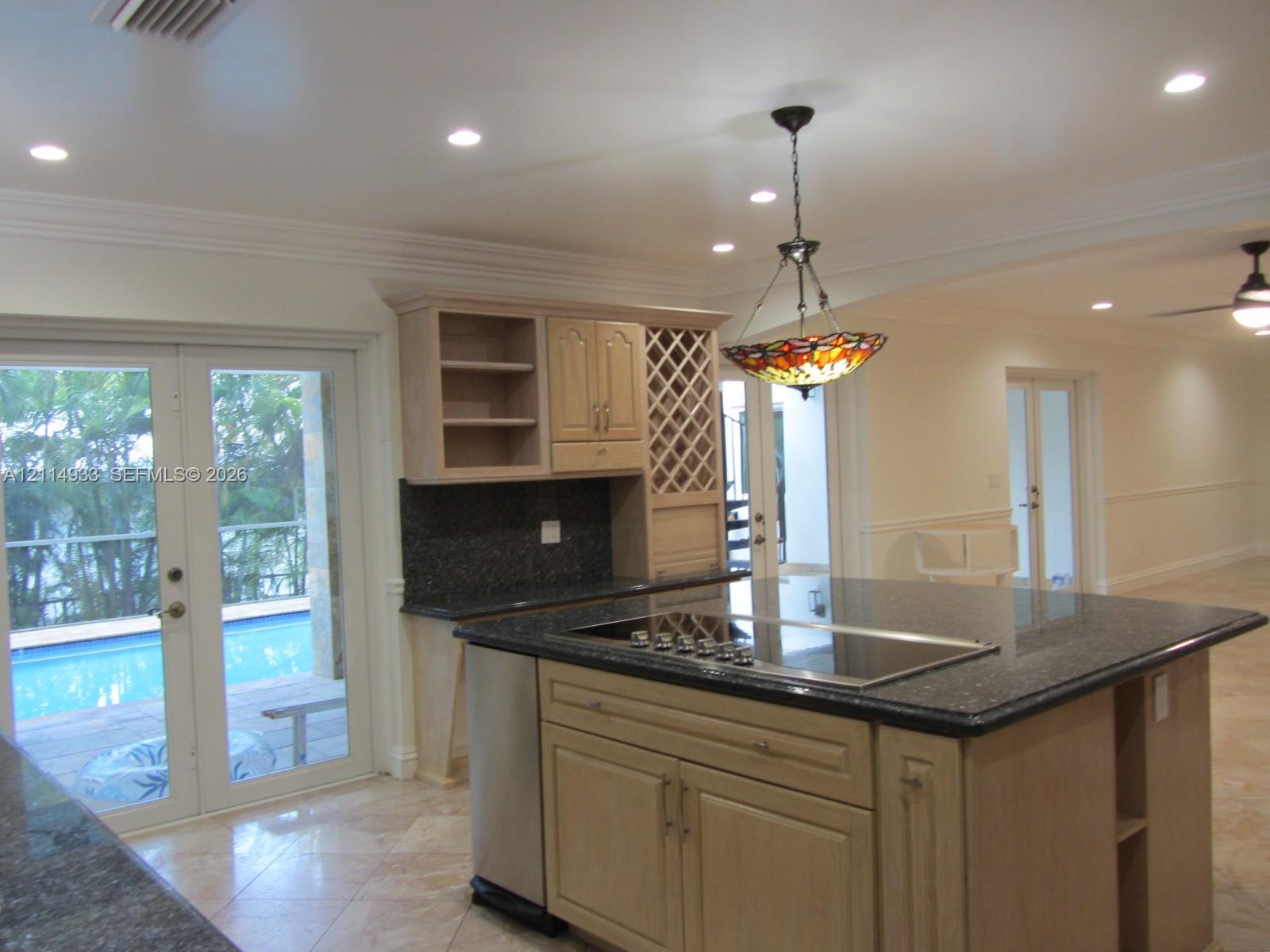 Kitchen featuring an expansive center island with a built-in cooktop, stone-finish countertops, custom wood cabinetry with integrated wine storage, and stone flooring throughout