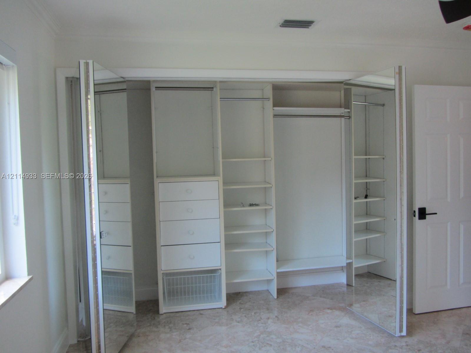 Custom reach-in closet featuring mirrored bi-fold doors, integrated shelving, multi-level hanging rods, and built-in drawer storage