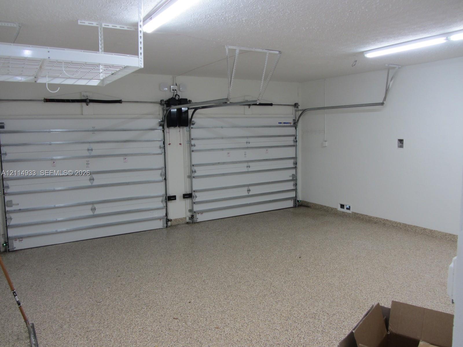 Two-car garage featuring dual overhead doors, overhead storage shelving, interior LED lighting, and speckled epoxy flooring
