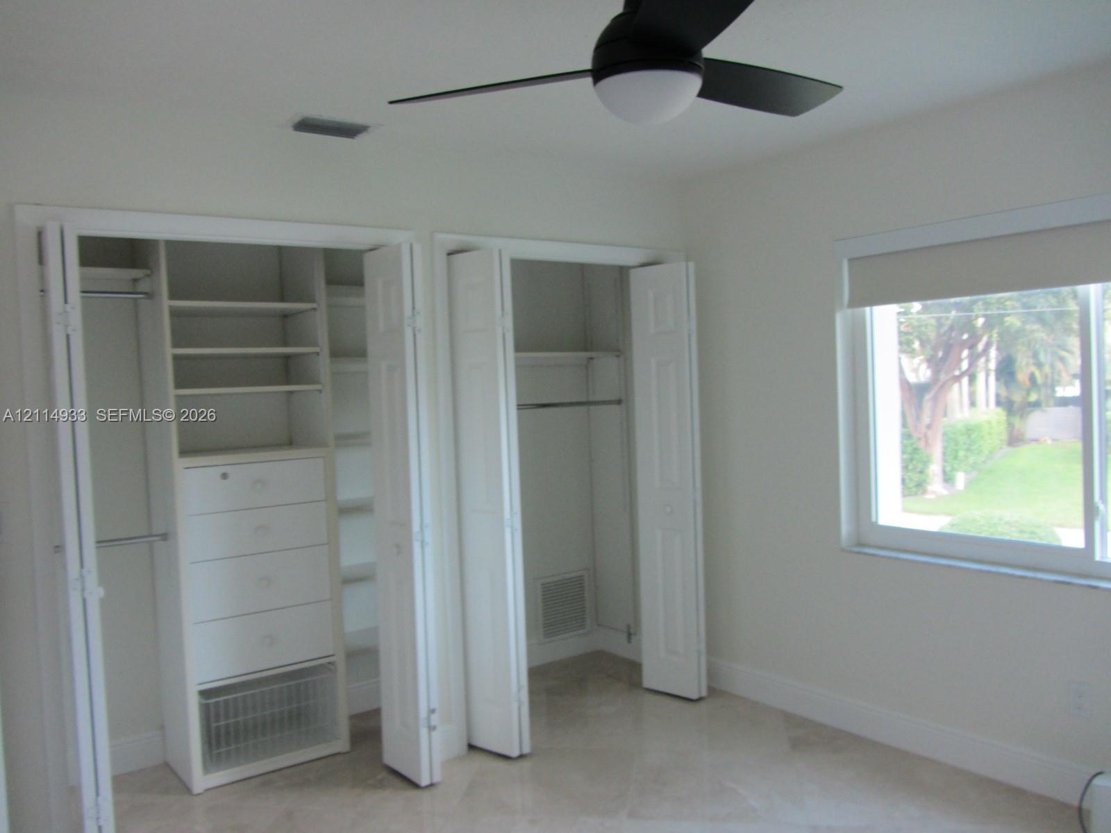 Dual closets with built-in shelving and integrated drawer storage, neutral tile flooring, and a ceiling fan with integrated light fixture