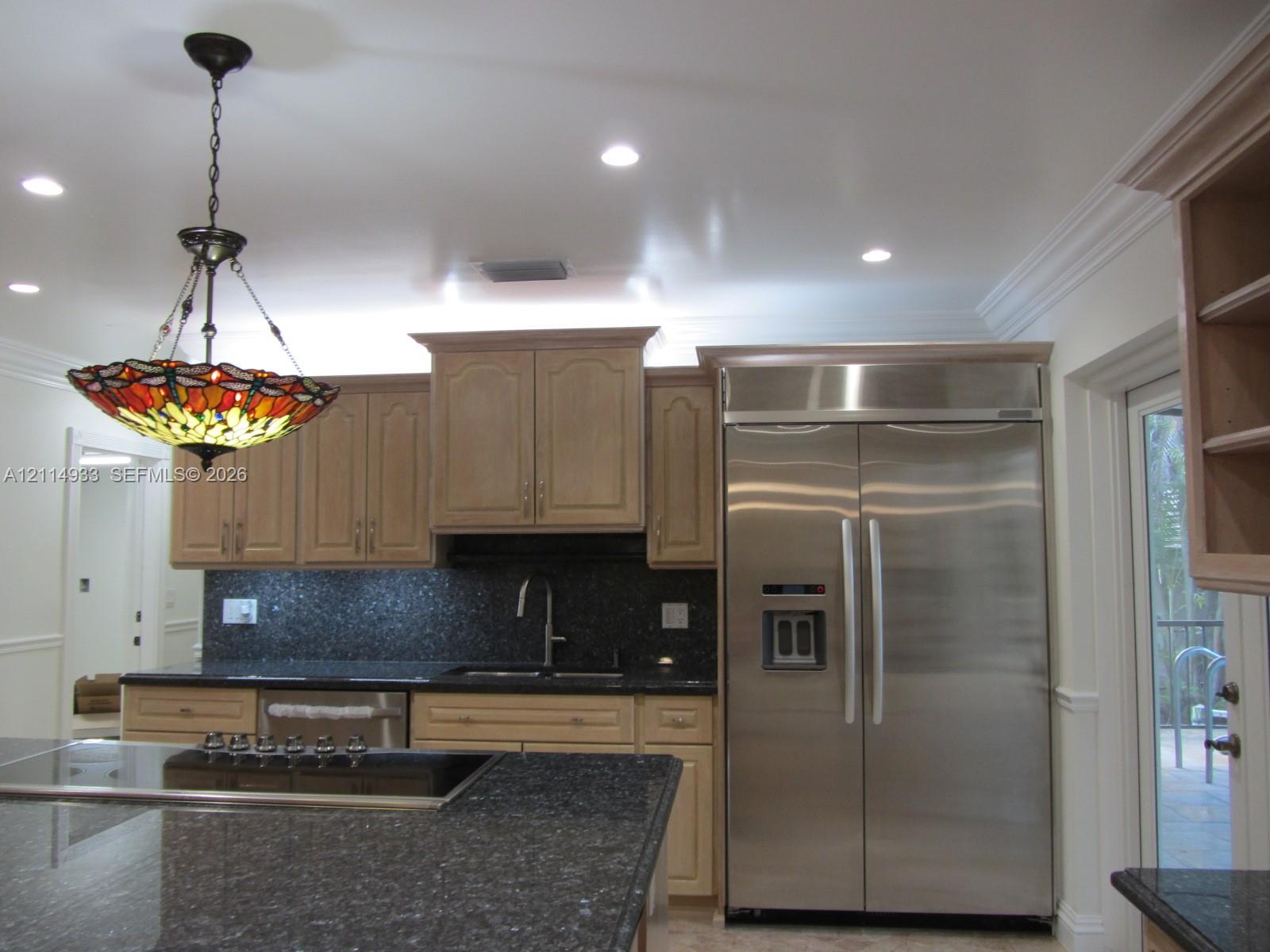 Kitchen featuring natural wood-finish cabinetry, dark stone countertops, recessed ceiling lighting, stainless steel side-by-side refrigerator, and a decorative stained glass pendant light