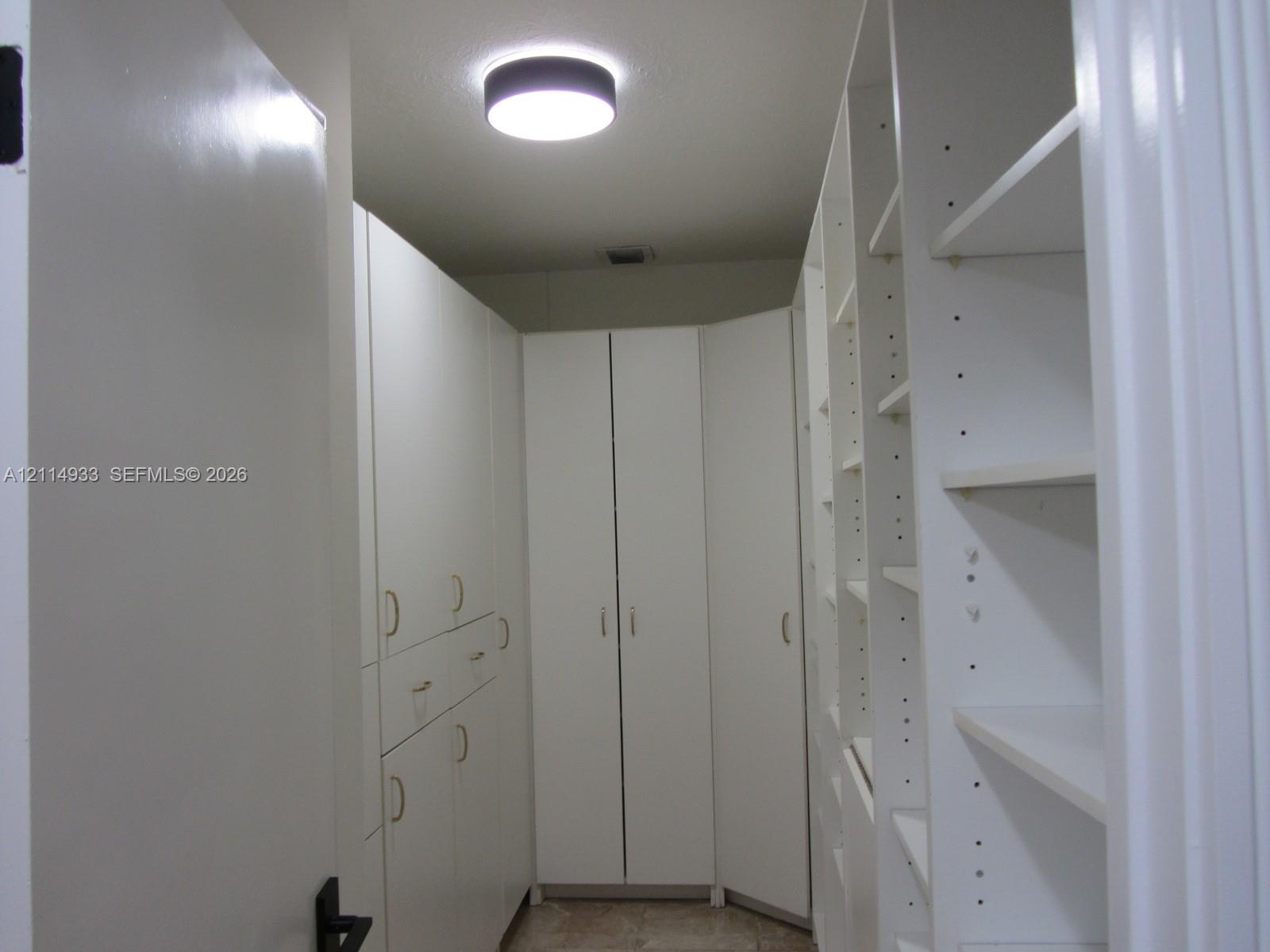 Custom floor-to-ceiling cabinetry featuring white laminate finish, adjustable shelving, integrated storage drawers, gold-toned hardware, and a circular flush-mount ceiling light