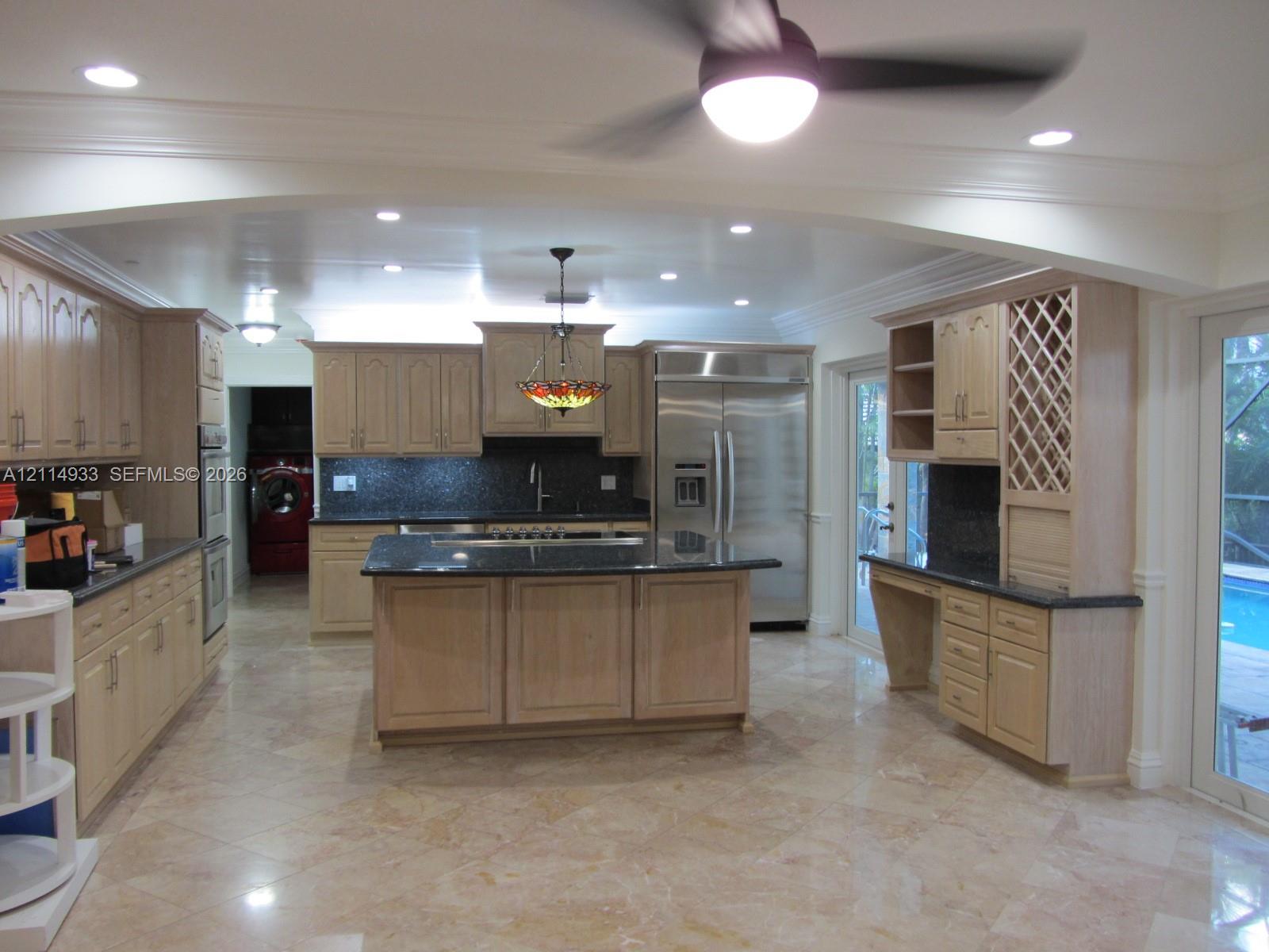 Kitchen featuring light wood cabinetry, center island, stone countertops, stainless steel appliances, and integrated wine rack