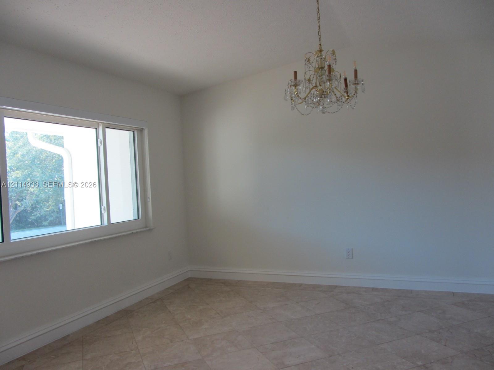 Vaulted ceiling, multi-light crystal chandelier, large-format tile flooring, and a wide horizontal window Vaulted ceiling, multi-light crystal chandelier, large-format tile flooring, and a wide horizontal window