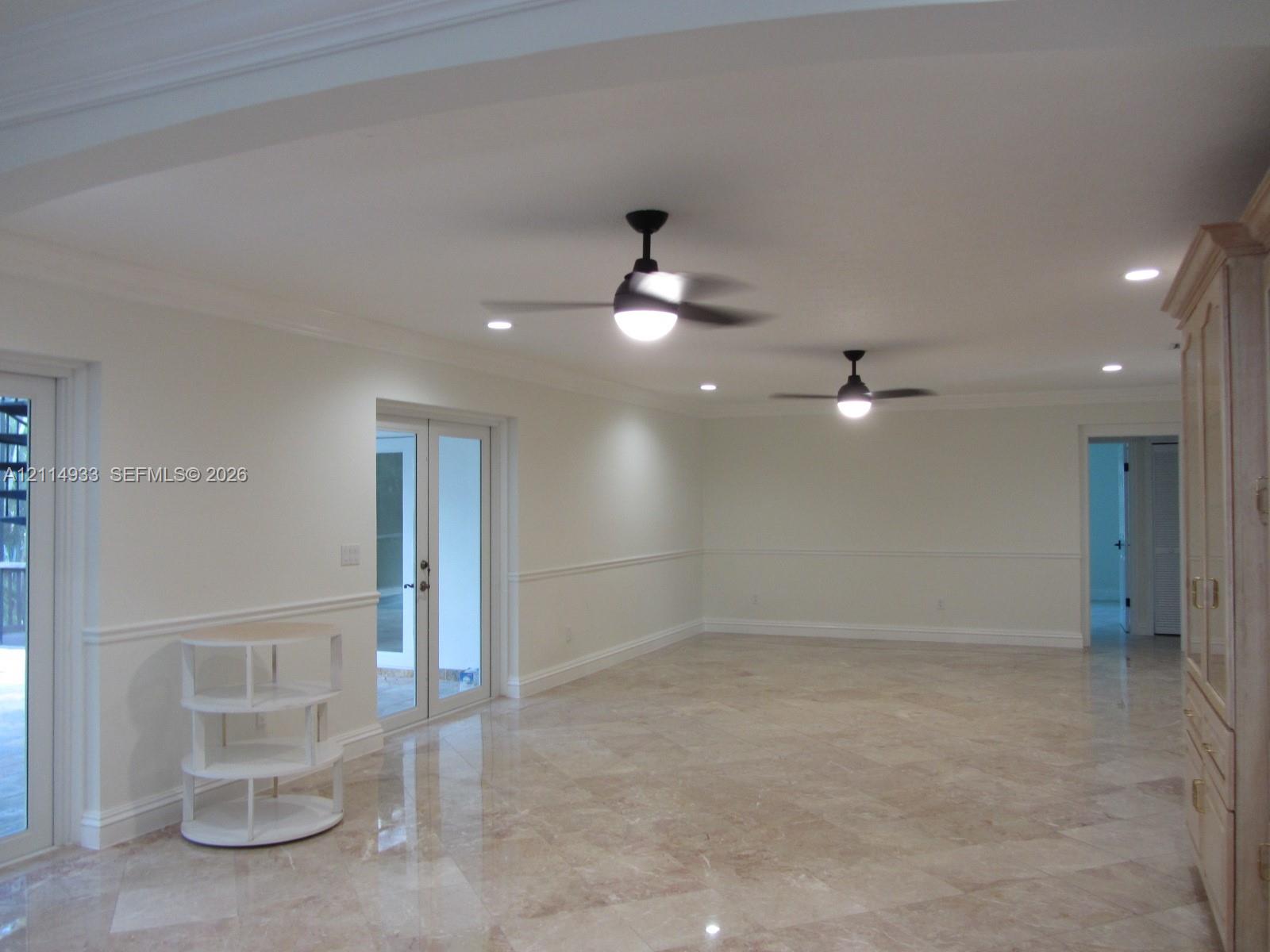 Polished stone flooring, crown molding, chair rail trim, dual ceiling fans with integrated lighting, and glass-paned French doors Polished stone flooring, crown molding, chair rail trim, dual ceiling fans with integrated lighting, and glass-paned French doors
