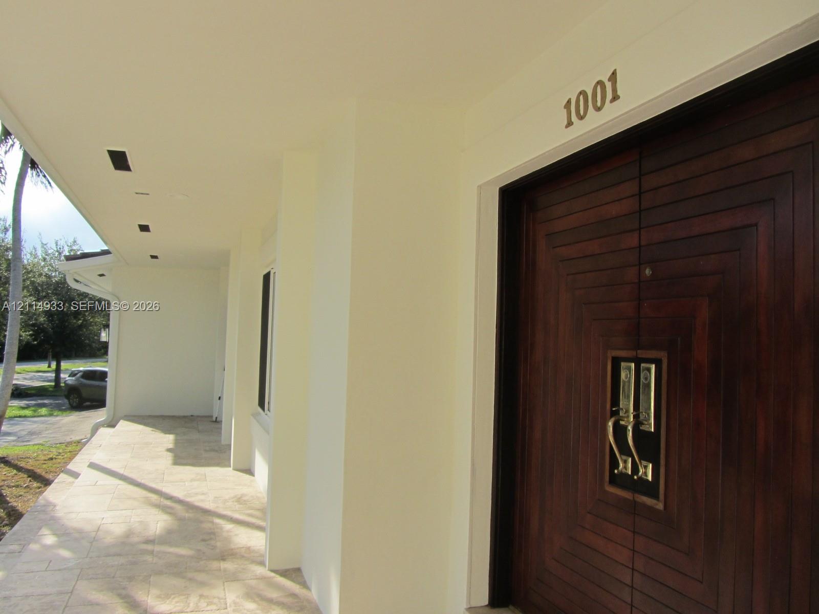 Covered entryway featuring natural stone tile flooring, recessed ceiling lighting, and double doors with dark wood finish and geometric relief detail Covered entryway featuring natural stone tile flooring, recessed ceiling lighting, and double doors with dark wood finish and geometric relief detail