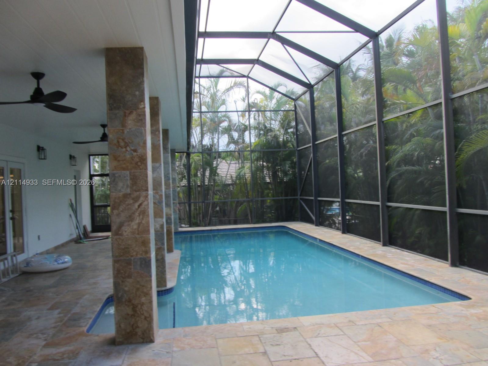 Screen-enclosed pool area featuring stone-tile decking, stone-clad structural pillars, recessed ceiling fans, and an attached covered patio Screen-enclosed pool area featuring stone-tile decking, stone-clad structural pillars, recessed ceiling fans, and an attached covered patio
